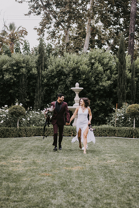  bride in a black gown with a black veil and the groom in a burgundy tuxedo with a black shirt and bow tie 