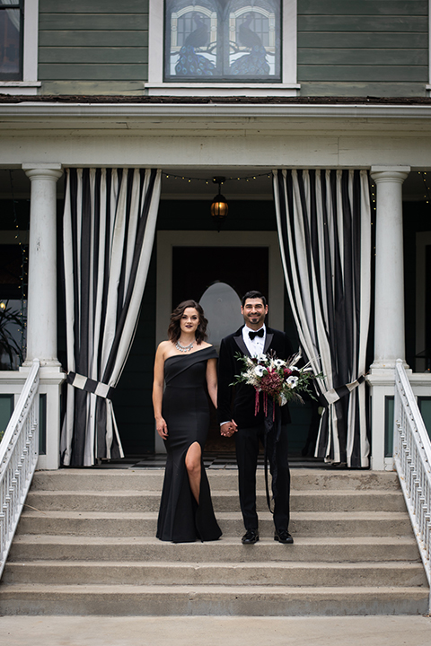  bride in a black gown with a black veil and the groom in a burgundy tuxedo with a black shirt and bow tie 