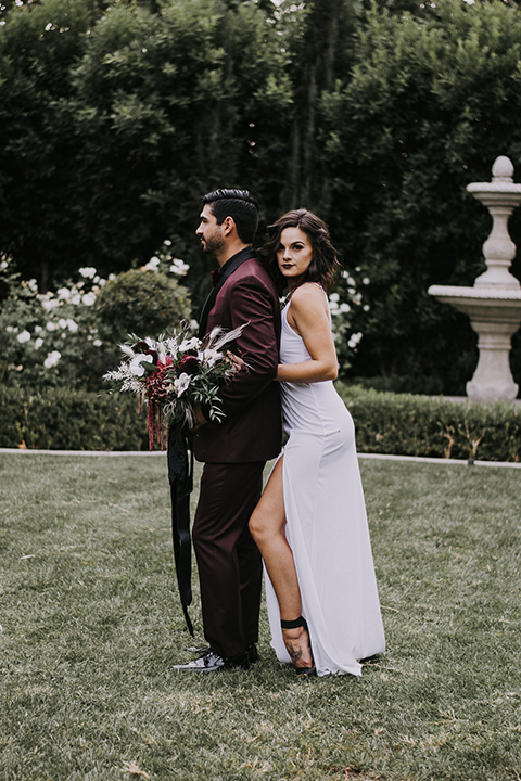  bride in a black gown with a black veil and the groom in a burgundy tuxedo with a black shirt and bow tie 