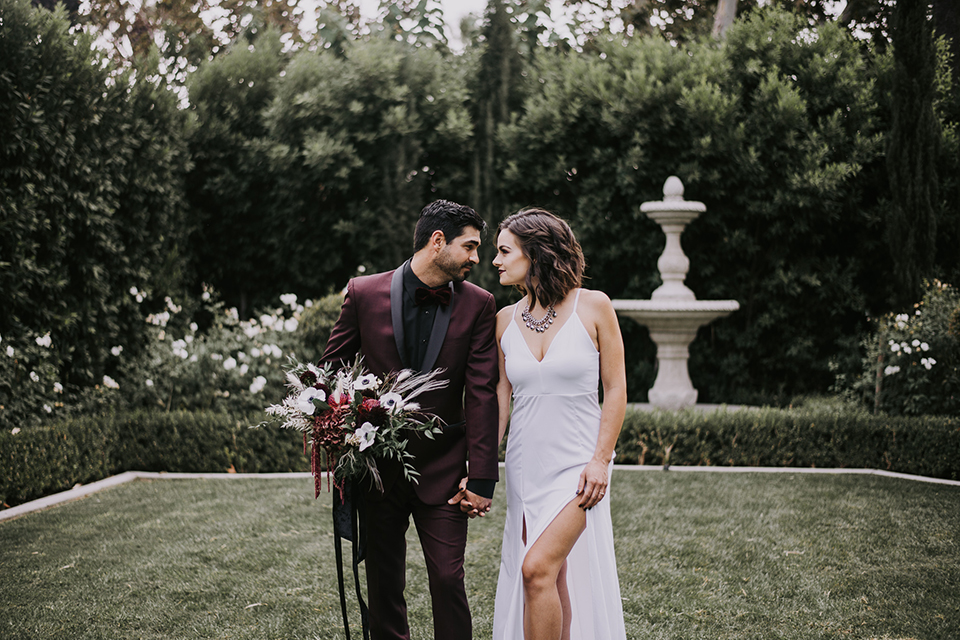  bride in a black gown with a black veil and the groom in a burgundy tuxedo with a black shirt and bow tie 