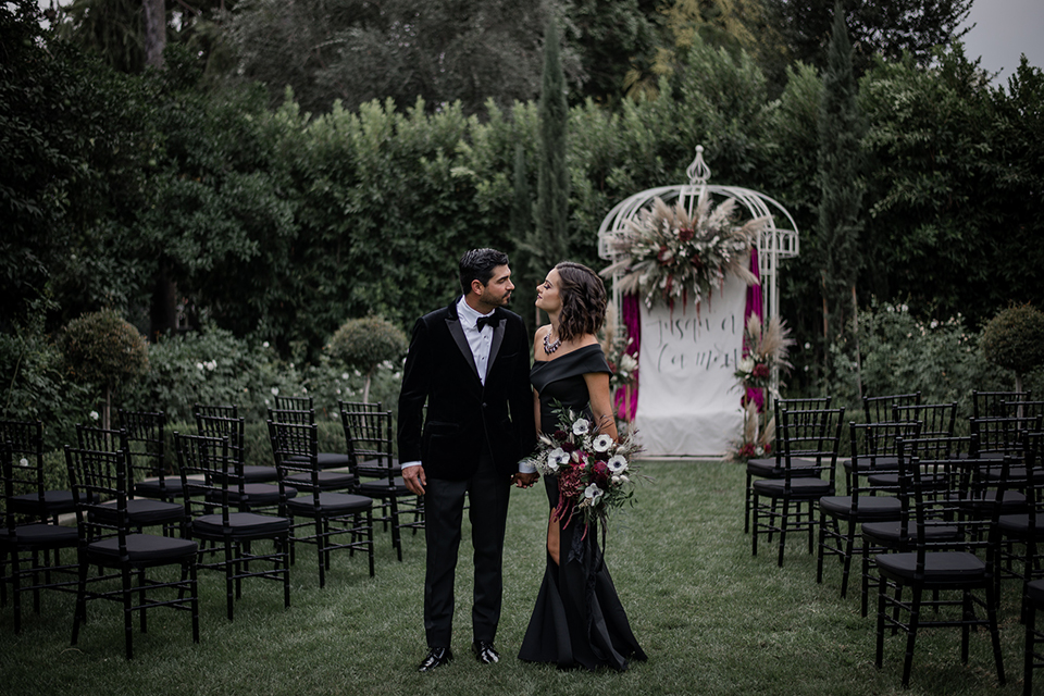  bride in a black gown with a black veil and the groom in a burgundy tuxedo with a black shirt and bow tie 