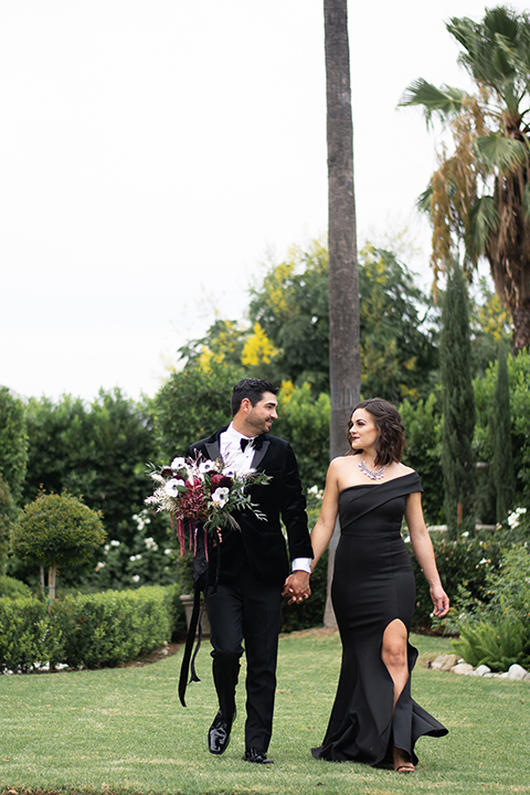  bride in a black gown with a black veil and the groom in a burgundy tuxedo with a black shirt and bow tie 