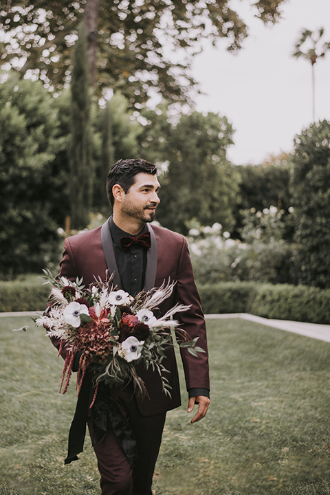  bride in a black gown with a black veil and the groom in a burgundy tuxedo with a black shirt and bow tie 