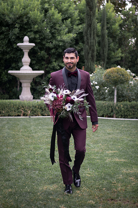  bride in a black gown with a black veil and the groom in a burgundy tuxedo with a black shirt and bow tie 