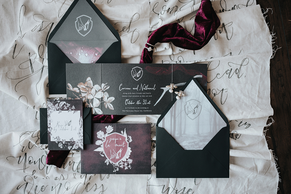  bride in a black gown with a black veil and the groom in a burgundy tuxedo with a black shirt and bow tie 