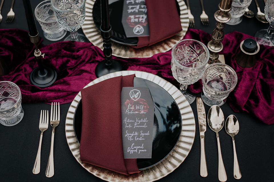  bride in a black gown with a black veil and the groom in a burgundy tuxedo with a black shirt and bow tie 