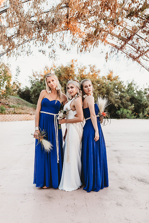  bride in a boho gown with her hair in a long french braid and the brides in royal blue gowns
