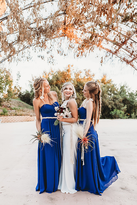  bride in a boho gown with her hair in a long french braid and the bridesmaids in royal blue gowns 
