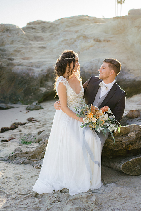  bride in  flowing gown with embellishments and the groom in a dark grey coat with light grey pants