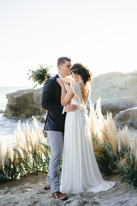  bride in  flowing gown with embellishments and the groom in a dark grey coat with light grey pants