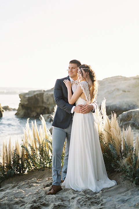   bride in  flowing gown with embellishments and the groom in a dark grey coat with light grey pants 