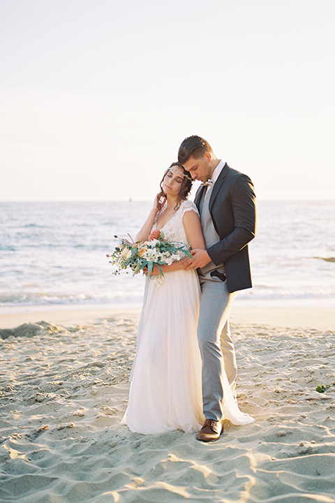   bride in  flowing gown with embellishments and the groom in a dark grey coat with light grey pants 