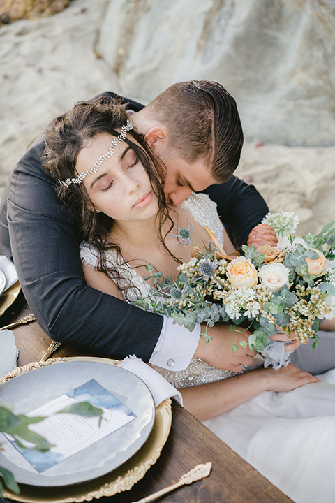   bride in  flowing gown with embellishments and the groom in a dark grey coat with light grey pants 