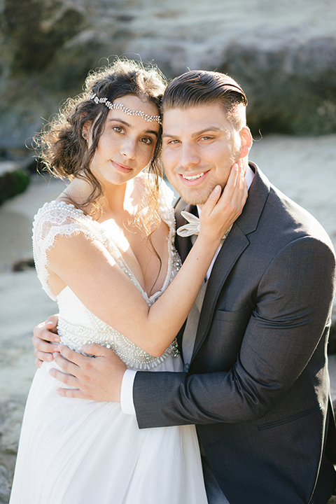   bride in  flowing gown with embellishments and the groom in a dark grey coat with light grey pants 