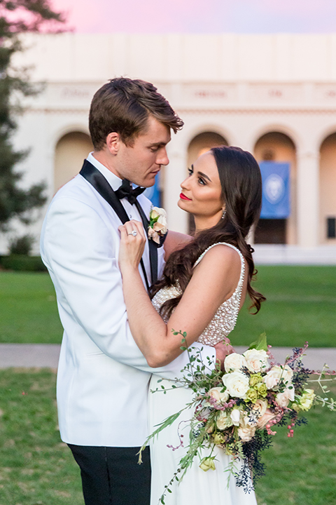  bride in a white modern gown with a high neck and cap sleeves, the groom in a white shawl lapel tuxedo and a black bow tie 