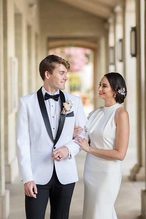  bride in a white modern gown with a high neck and cap sleeves, the groom in a white shawl lapel tuxedo and a black bow tie 