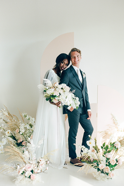  bride in a white formfitting modern gown and cape and the groom in a slate blue suit with a silver long tie 