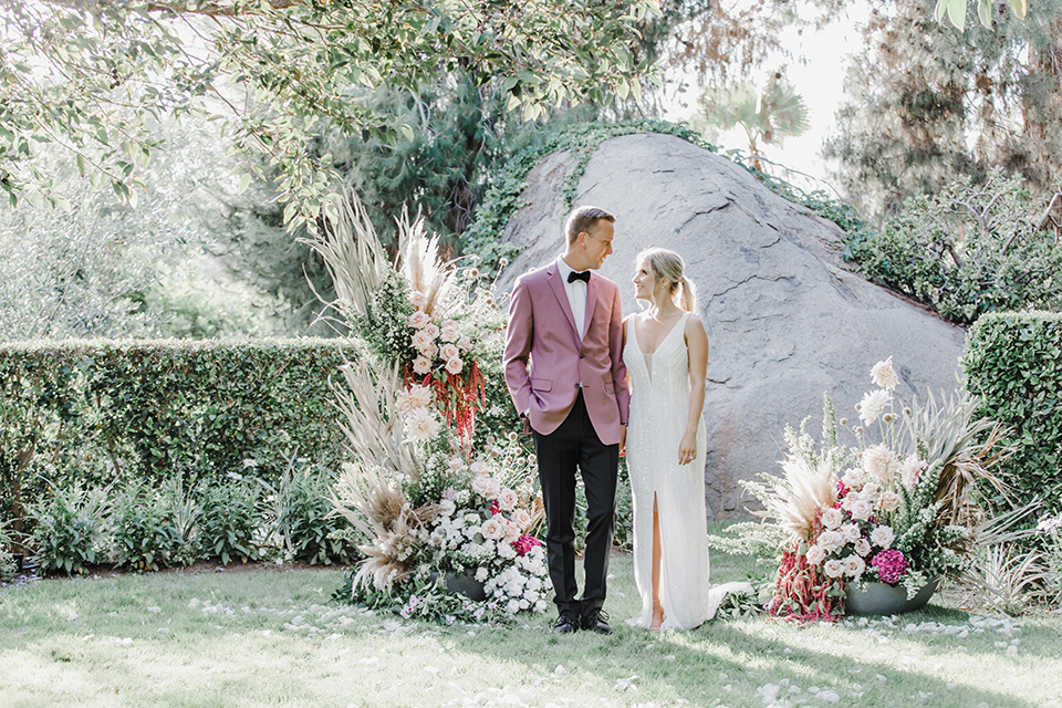  the bride and groom at the reception – the bride in a white lace gown and the groom in a rose pink coat and black pants 