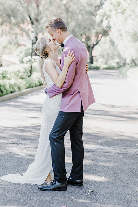  the bride and groom at the reception – the bride in a white lace gown and the groom in a rose pink coat and black pants 