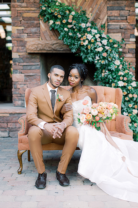  red rocks caramel wedding couple sitting – bride in a strapless modern gown and the groom in a caramel tan suit with a chocolate brown tie