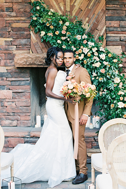  red rocks caramel wedding couple sitting – bride in a strapless modern gown and the groom in a caramel tan suit with a chocolate brown tie