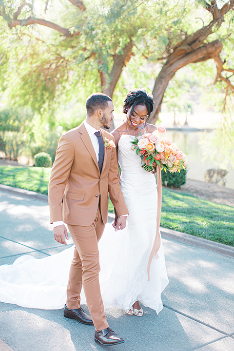  red rocks caramel wedding couple sitting – bride in a strapless modern gown and the groom in a caramel tan suit with a chocolate brown tie