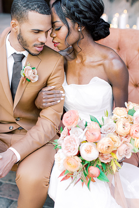  red rocks caramel wedding couple sitting – bride in a strapless modern gown and the groom in a caramel tan suit with a chocolate brown tie 