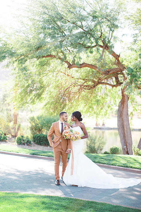  red rocks caramel wedding couple sitting – bride in a strapless modern gown and the groom in a caramel tan suit with a chocolate brown tie 