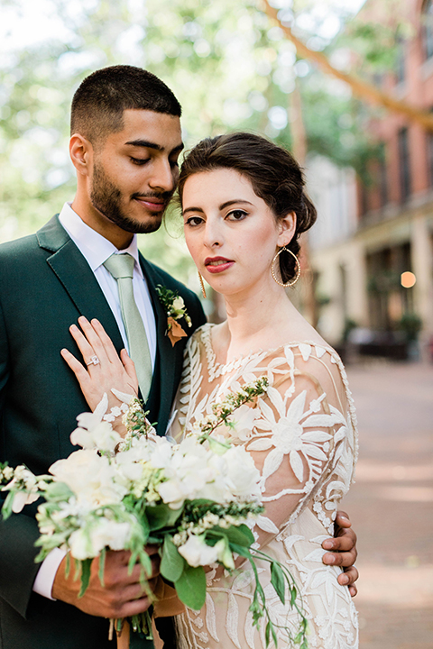  bride in an ivory lace gown with modern style design and a high neckline and long sleeves, the groom in a dark green suit with a black and white plaid tie 