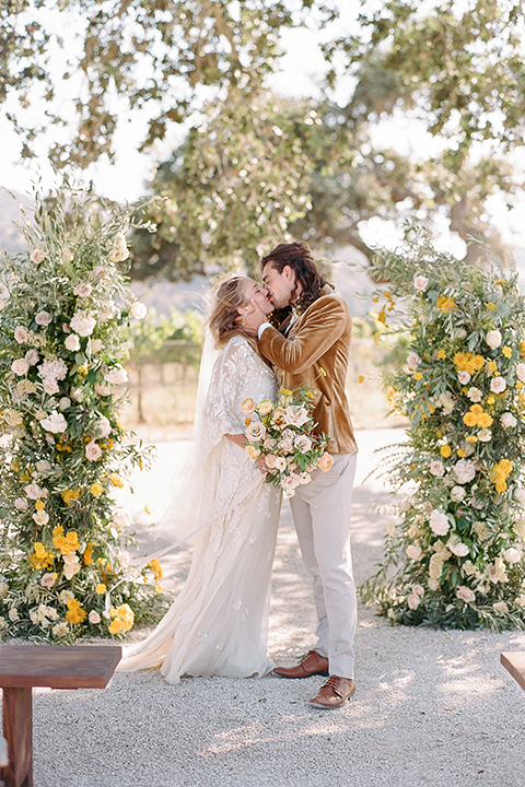  the bride in a lace flowing gown with bell sleeves and the groom in a gold velvet tuxedo