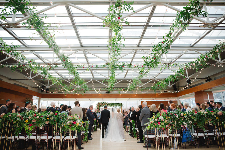  groom in a green suit with a pink floral bow tie and bride in a white a line gown with colorful flowers 