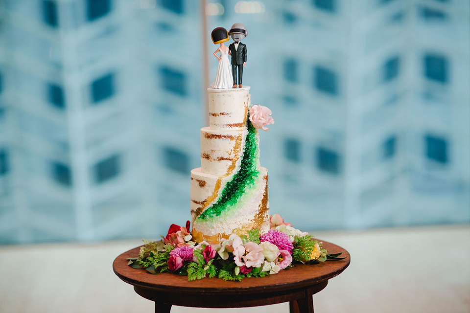  groom in a green suit with a pink floral bow tie and bride in a white a line gown with colorful flowers 