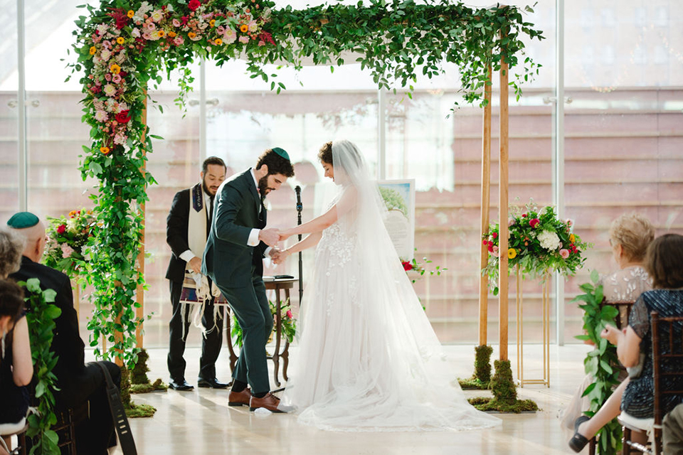  groom in a green suit with a pink floral bow tie and bride in a white a line gown with colorful flowers 