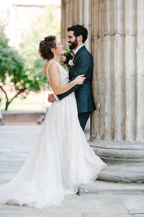  groom in a green suit with a pink floral bow tie and bride in a white a line gown with colorful flowers 