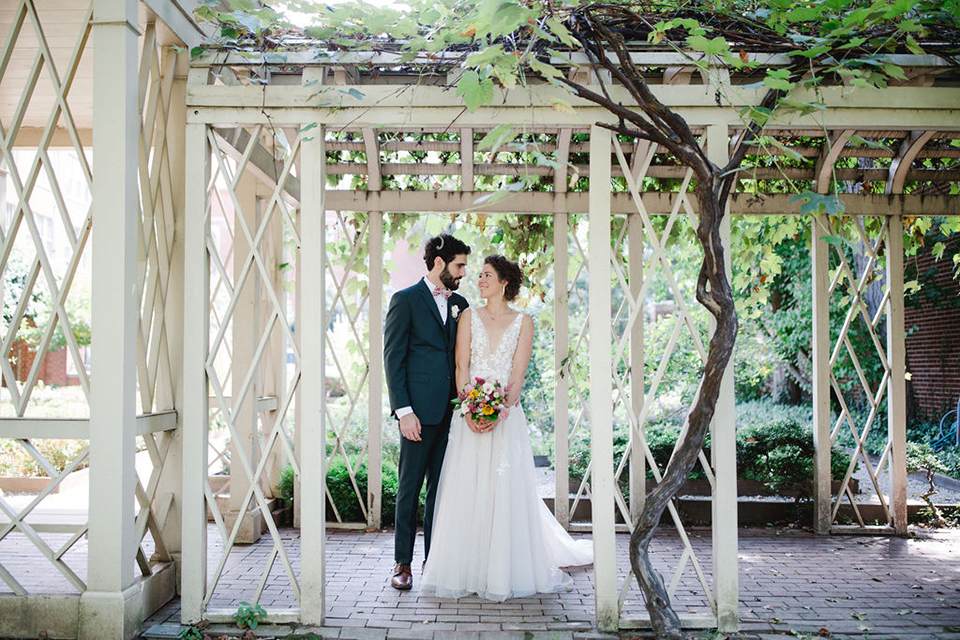  groom in a green suit with a pink floral bow tie and bride in a white a line gown with colorful flowers 