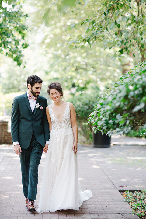  groom in a green suit with a pink floral bow tie and bride in a white a line gown with colorful flowers 