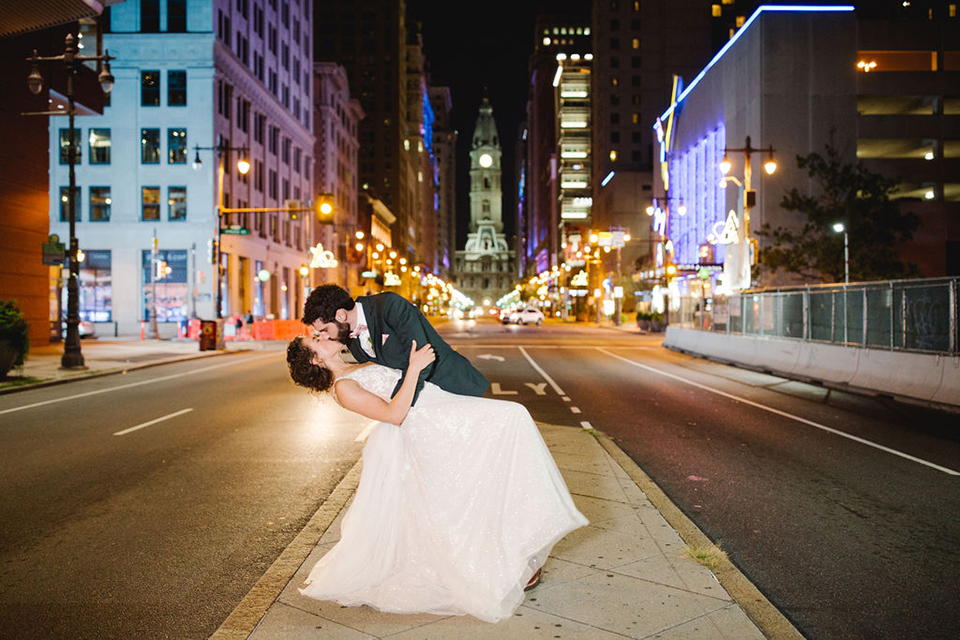  groom in a green suit with a pink floral bow tie and bride in a white a line gown with colorful flowers 