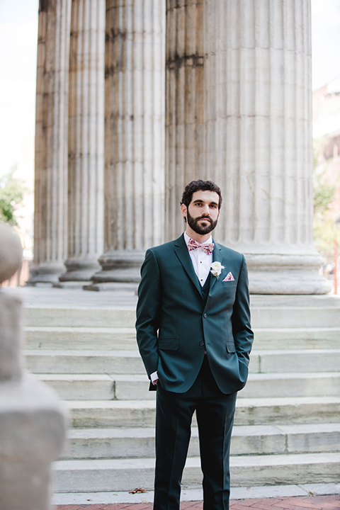  groom in a green suit with a pink floral bow tie and bride in a white a line gown with colorful flowers 