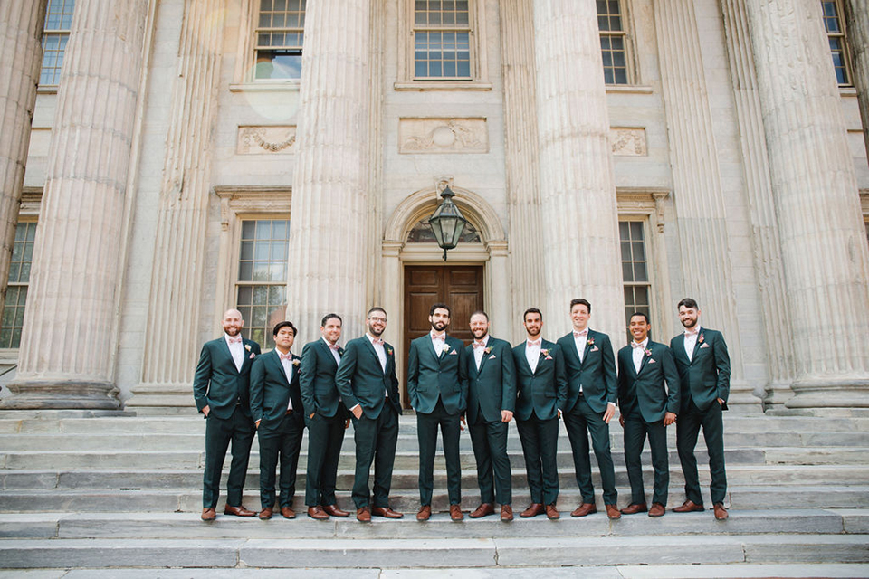  groom in a green suit with a pink floral bow tie and bride in a white a line gown with colorful flowers 