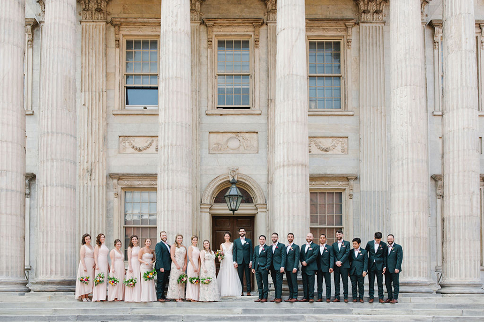  groom in a green suit with a pink floral bow tie and bride in a white a line gown with colorful flowers 