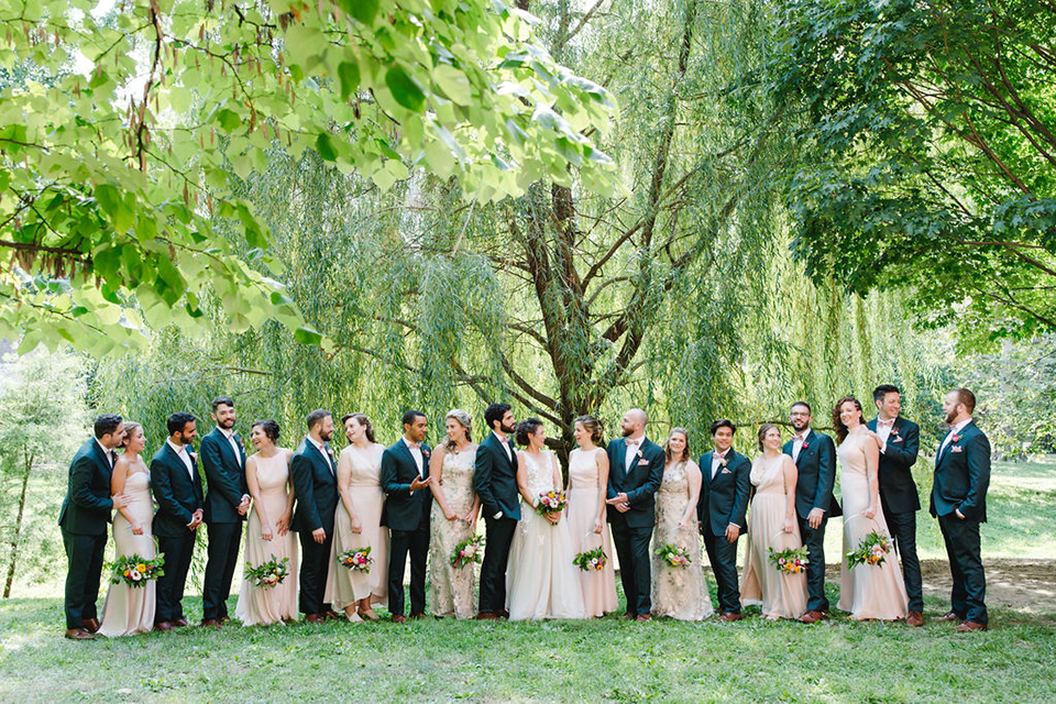  groom in a green suit with a pink floral bow tie and bride in a white a line gown with colorful flowers 