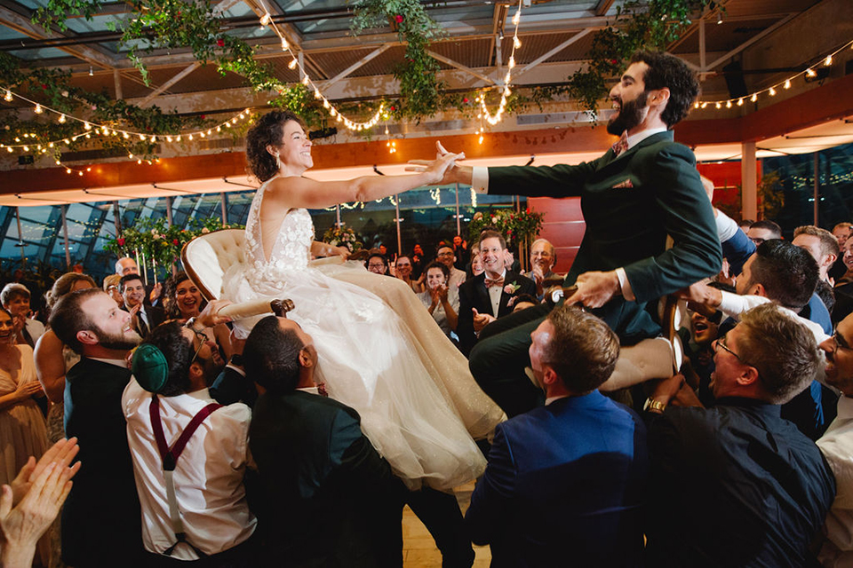  groom in a green suit with a pink floral bow tie and bride in a white a line gown with colorful flowers 