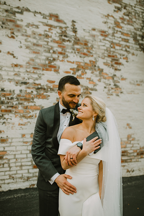  bride in an off the shoulder modern gown and the groom in a charcoal shawl lapel tuxedo 