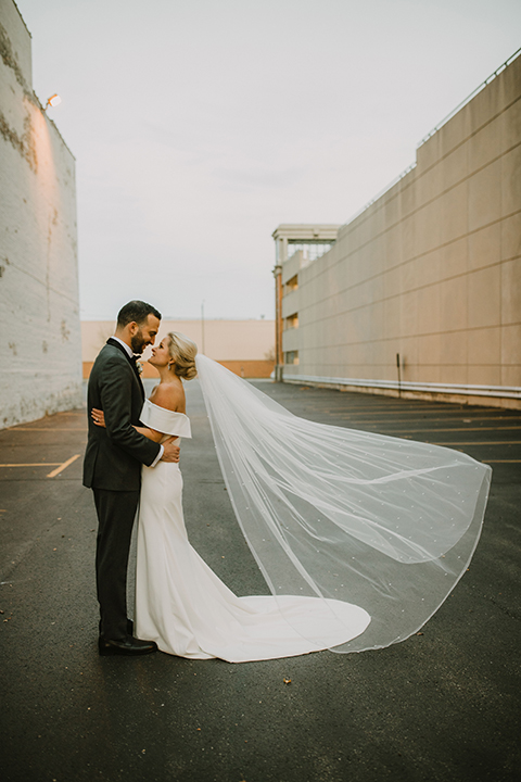  bride in an off the shoulder modern gown and the groom in a charcoal shawl lapel tuxedo 