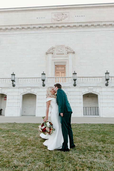  bride in a trumpet style gown and the groom in a green suit, the groomsmen in caramel notch lapel suits and the bridesmaids in ivory gowns 