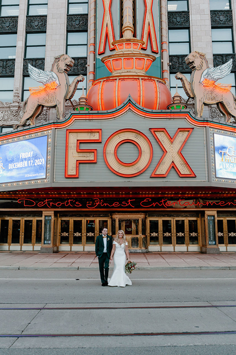  bride in a trumpet style gown and the groom in a green suit, the groomsmen in caramel notch lapel suits and the bridesmaids in ivory gowns 