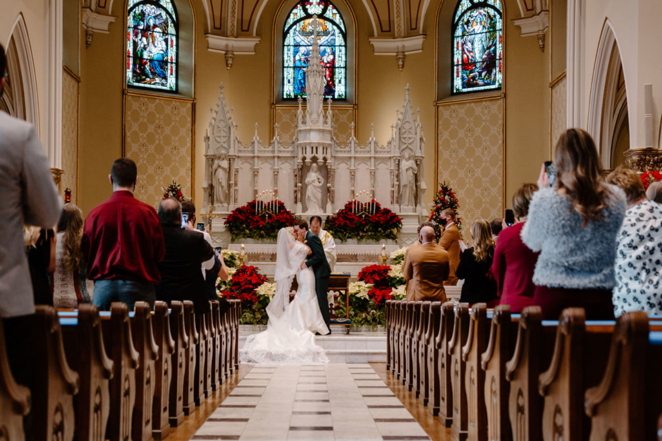  bride in a trumpet style gown and the groom in a green suit, the groomsmen in caramel notch lapel suits and the bridesmaids in ivory gowns 