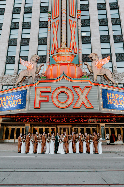  bride in a trumpet style gown and the groom in a green suit, the groomsmen in caramel notch lapel suits and the bridesmaids in ivory gowns 