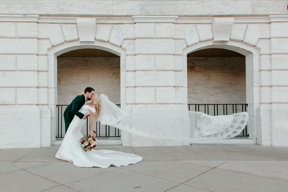  bride in a trumpet style gown and the groom in a green suit, the groomsmen in caramel notch lapel suits and the bridesmaids in ivory gowns 