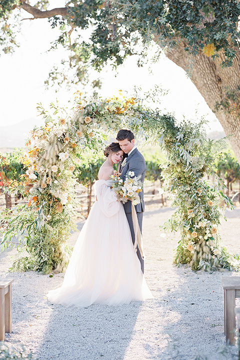  wedding at sunstone winery with romantic details and the groom in a café brown suit and the bride in a flowing ballgown with billowing sleeves 